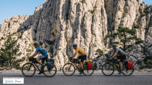 Cicloturismo en la Marina Alta: tres ciclistas rodando por carretera de montaña con pared de roca caliza al fondo en la Costa Blanca Norte